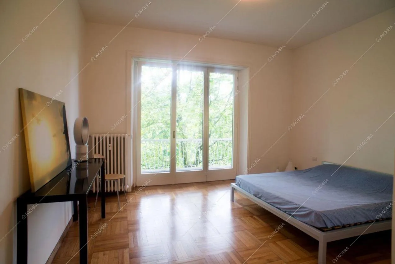 Camera da letto matrimoniale minimal con pavimento in parquet e accesso al balcone tramite porte-finestre