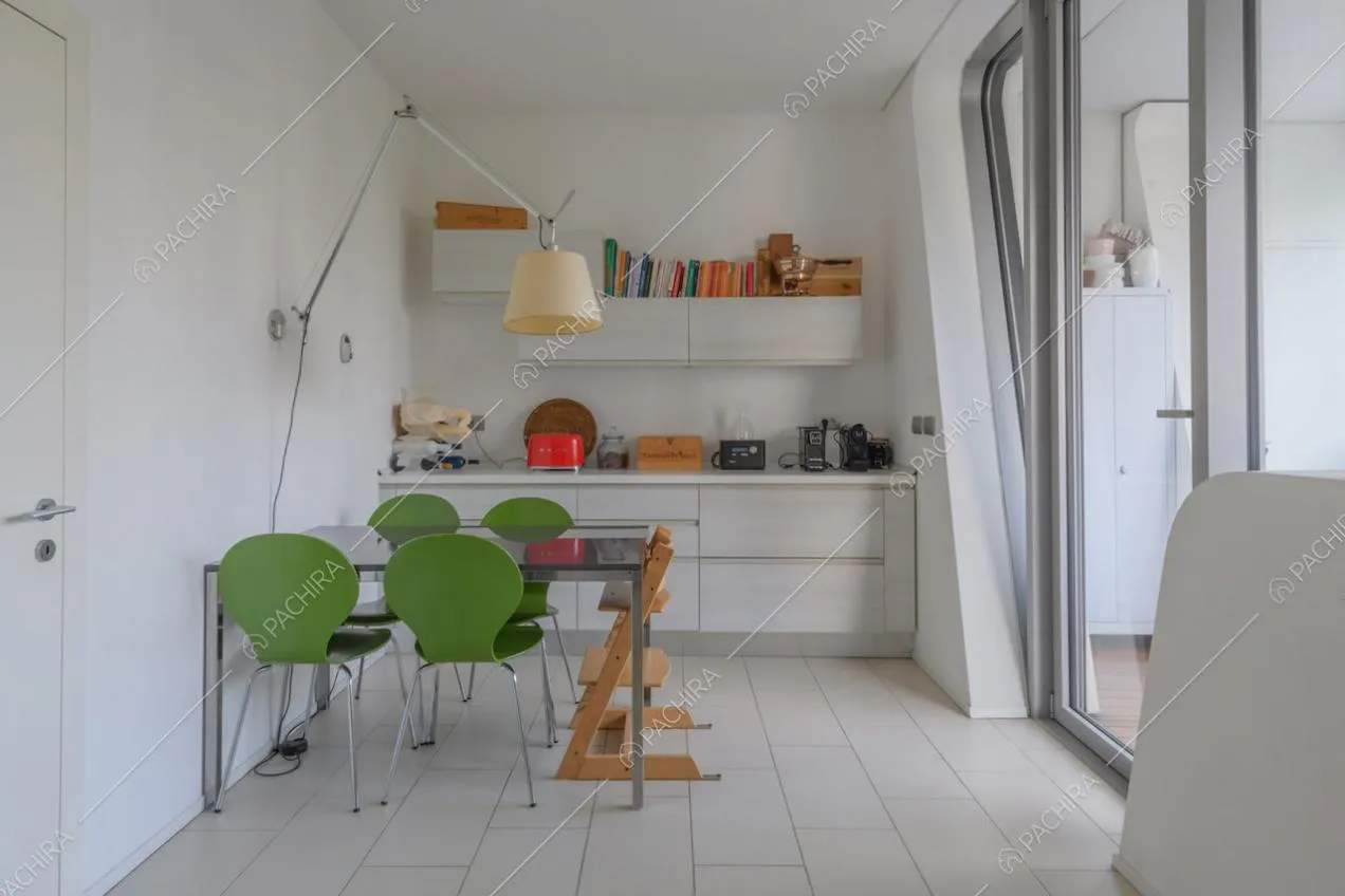 Cucina bianca a parete con tavolo da pranzo nero, sedie verdi e porta-finestra