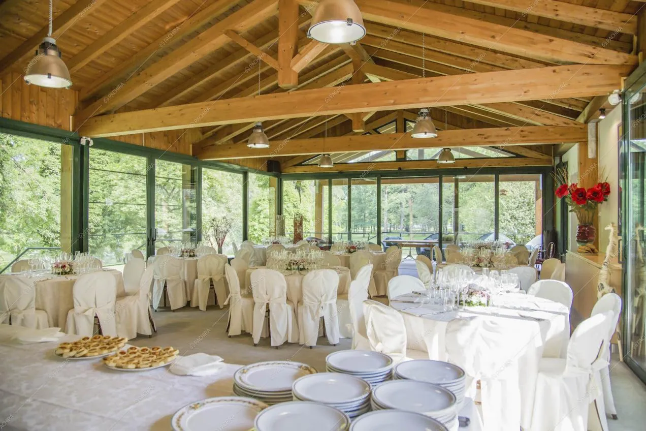 Tavoli bianchi da ricevimento nell'ampio salone circondato da vetrate e con soffitto in legno