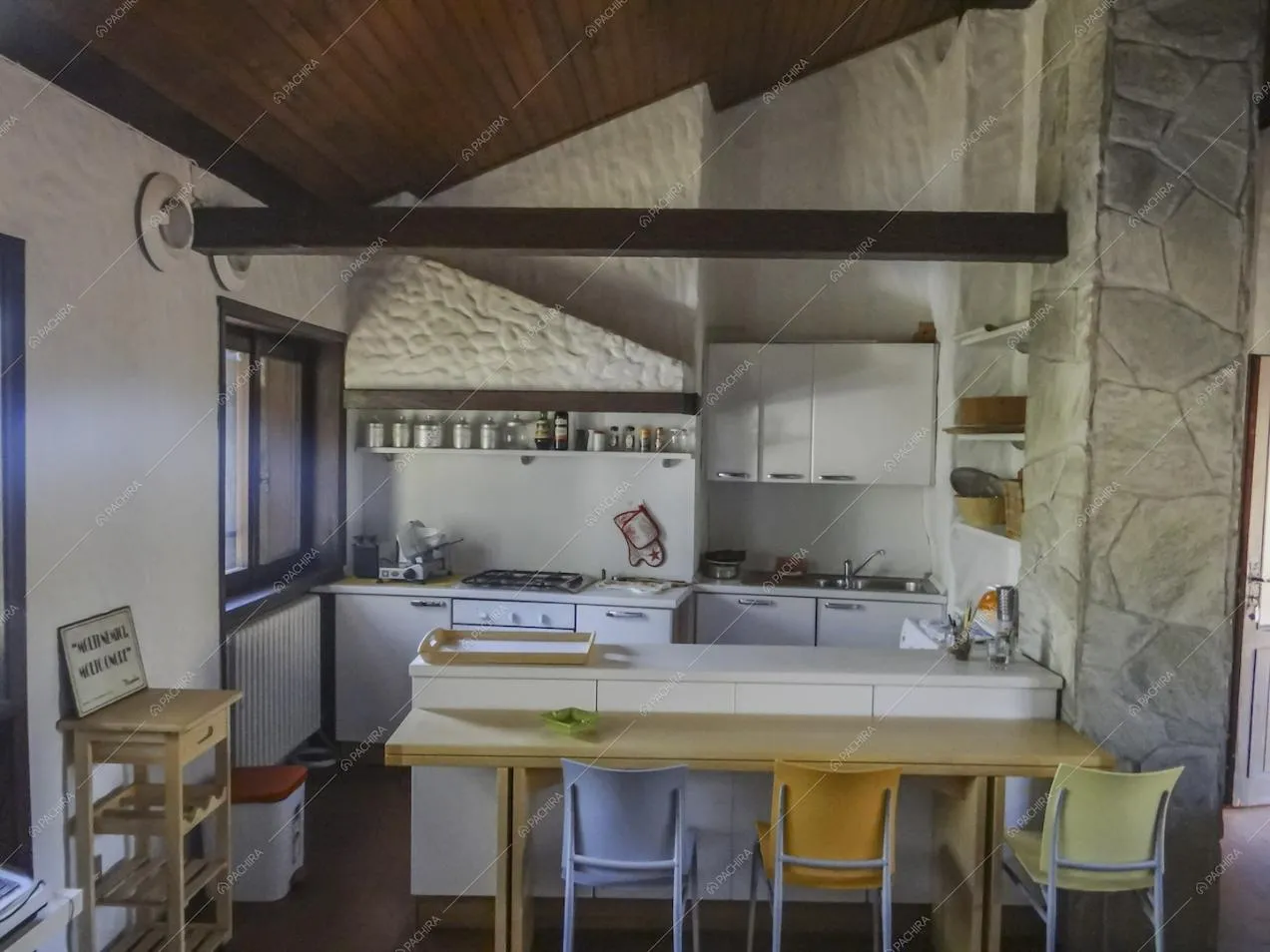 Cucina bianca a muro con fornelli a gas e soffitto in legno a vista