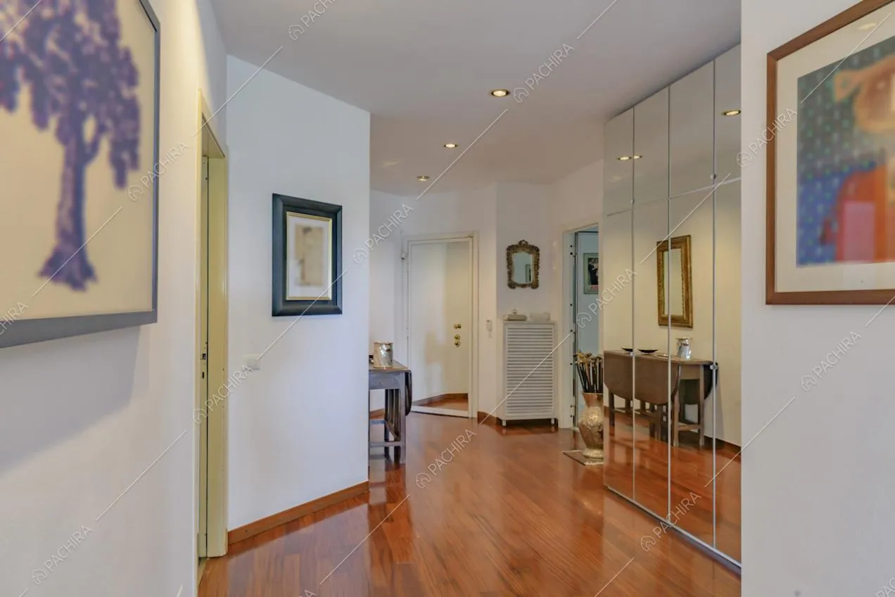Corridoio dalle pareti bianche e pavimento in parquet si affaccia su un armadio a muro a specchio