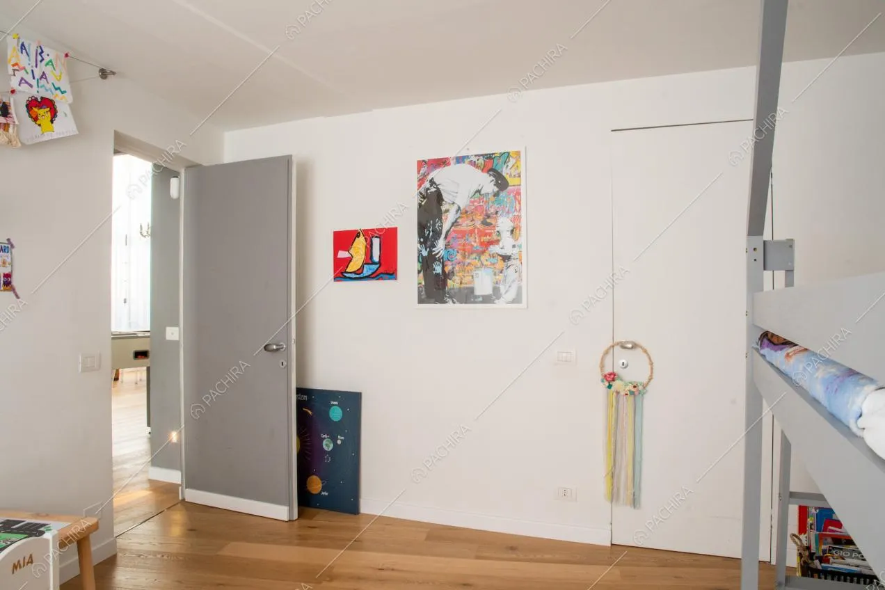 Dalla camera da letto da bambini, con pareti bianche e pavimento in parquet, vista sul soggiorno