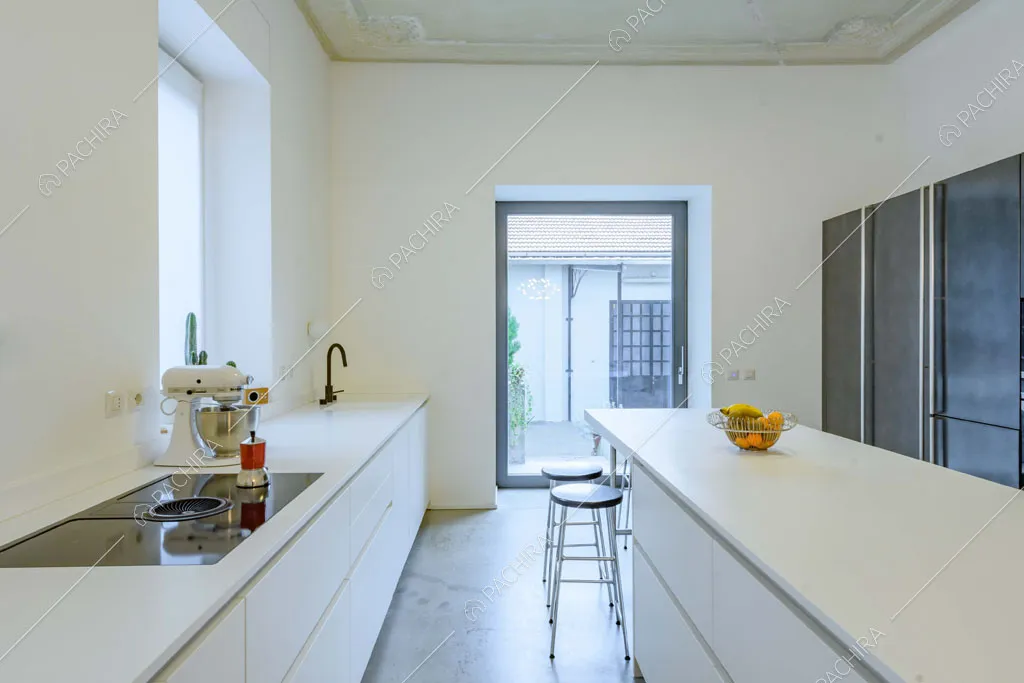 Cucina con isola bianca, boiserie sul soffitto, porta-finestra e fornelli a induzione