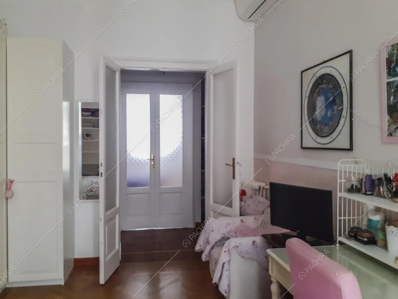 Parete bianca e rosa, armadio bianco, poltrona e televisione nella cameretta