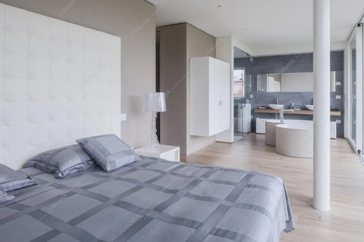 Nella camera dalle pareti beige, letto matrimoniale con testata bianca e vista sulla vasca dalla forma ondulata