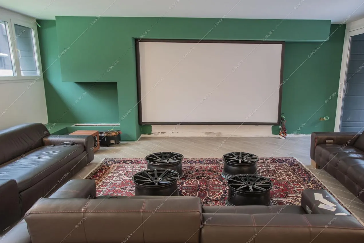 Sala cinema con parete verde scuro, divani marroni in pelle e cerchioni come tavolini
