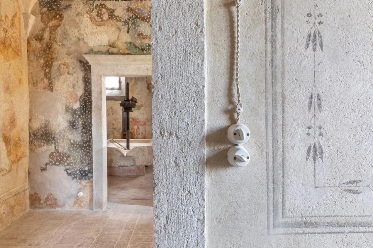 Dal corridoio con le mura affrescate e pavimento in cotto scorcio sul torchio della cucina