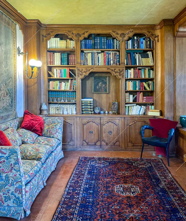 Studio con libreria con boiserie, arazzo, divano a fantasia floreale e pavimento in cotto