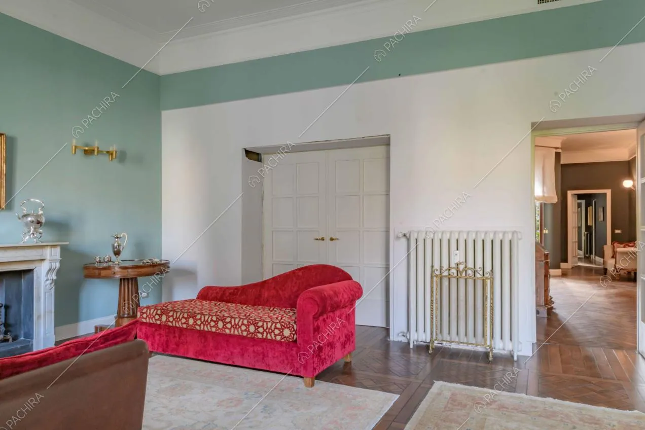 Sala con divani rossi in velluto, pareti azzurre e bianche, camino e vista sul corridoio
