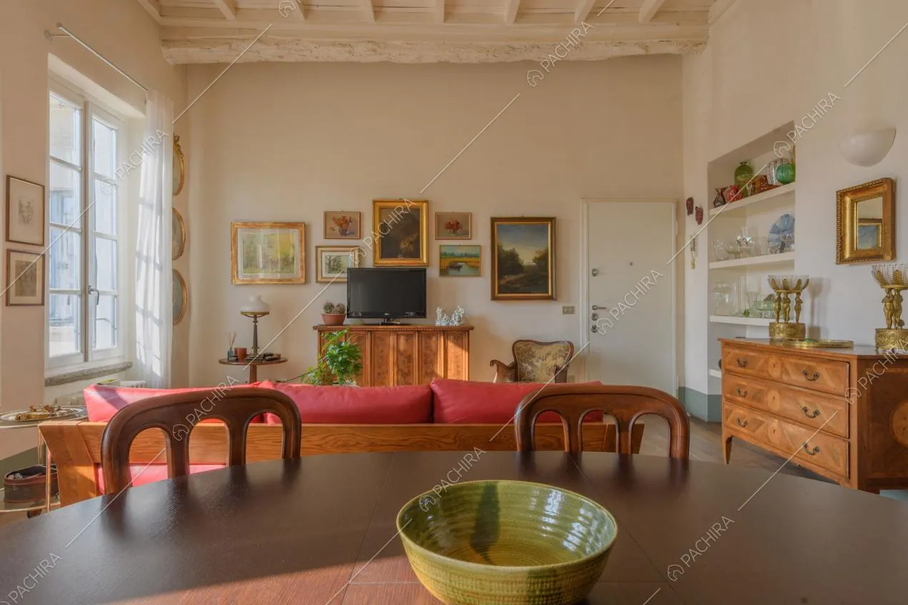 Dal tavolo da pranzo in legno vista sul divano rosso e sulle pareti bianche della zona living