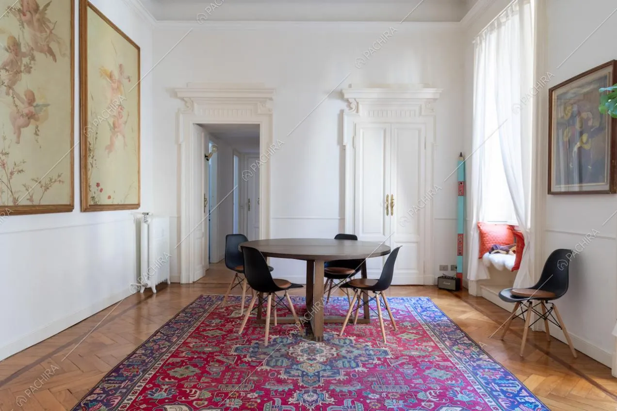 Vista sul tavolo da pranzo in legno nell'ampia stanza con boiserie alle pareti bianche