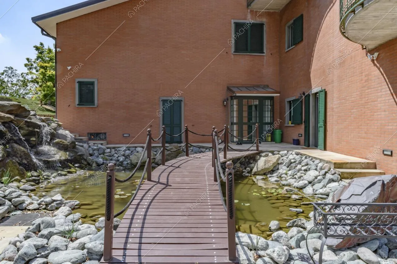 Ponte di legno sul laghetto con sassi della locaiton, che porta a uno degli ingressi con pergolato