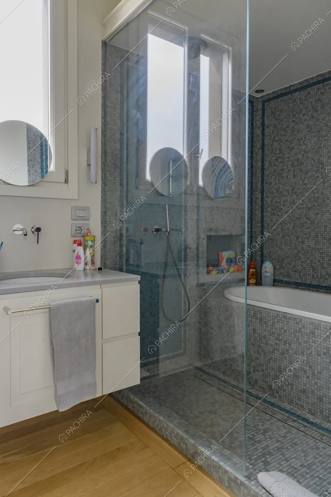 Bagno con pavimento in parquet e vasca separata da una parete in vetro