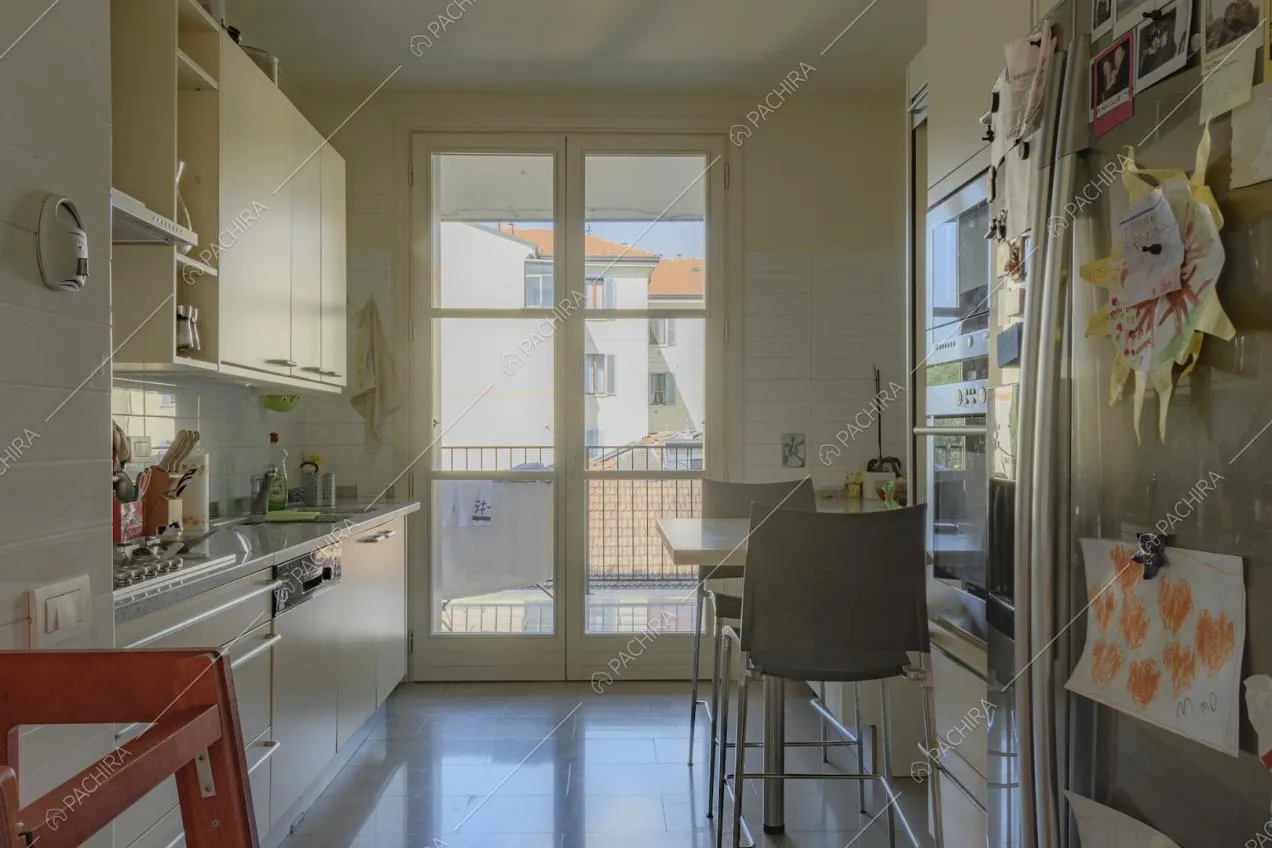Porta finestra, tavolo con sedie alte e mobili da cucina chiari