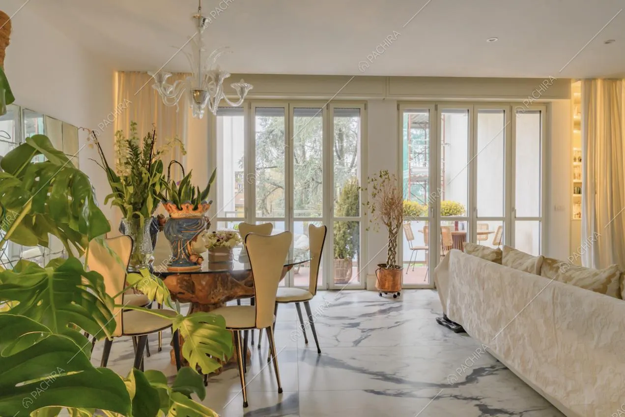 Salotto della location con pavimento in marmo, porte-finestre per accedere al balcone e lampadario bianco 