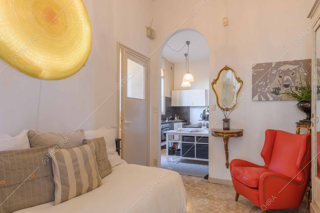 Divano bianco, poltrona rossa e pareti bianche nella stanza con vista sulla cucina