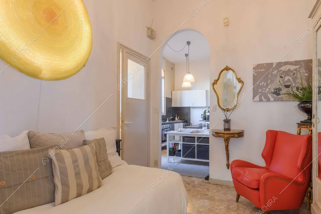Divano bianco, poltrona rossa e pareti bianche nella stanza con vista sulla cucina