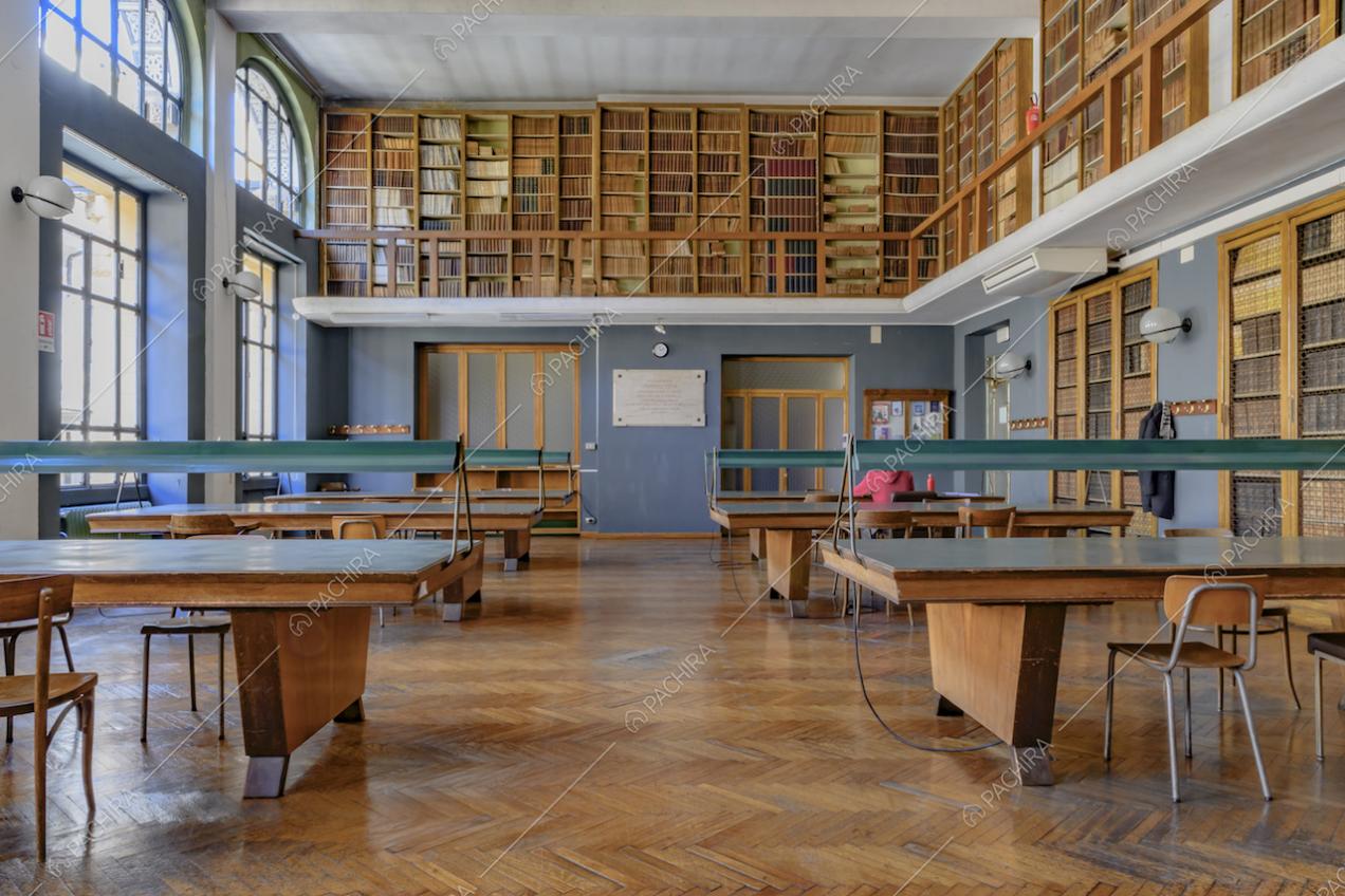 Luminosa biblioteca con tavolo in legno per la consultazione, balconata con librerie e pareti azzurre