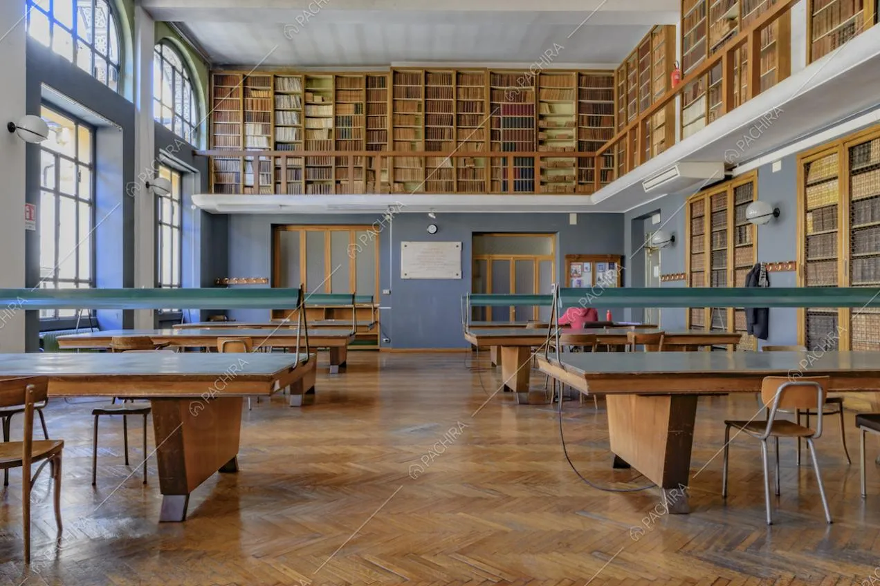 Luminosa biblioteca con tavolo in legno per la consultazione, balconata con librerie e pareti azzurre