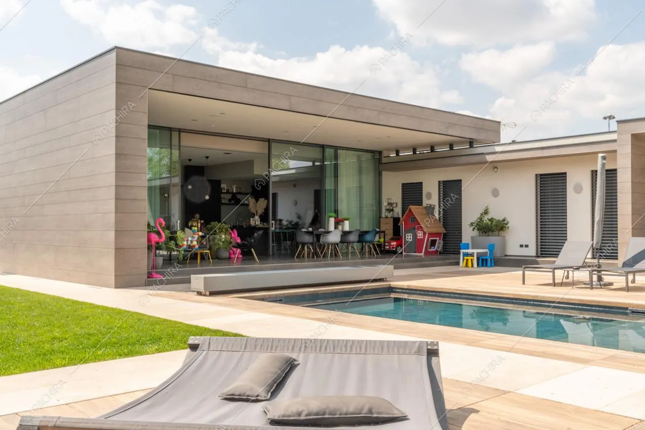 Dalla sdraio nel giardino vista sulla piscina, sui lettini e sulla zona living della location attraverso le vetrate