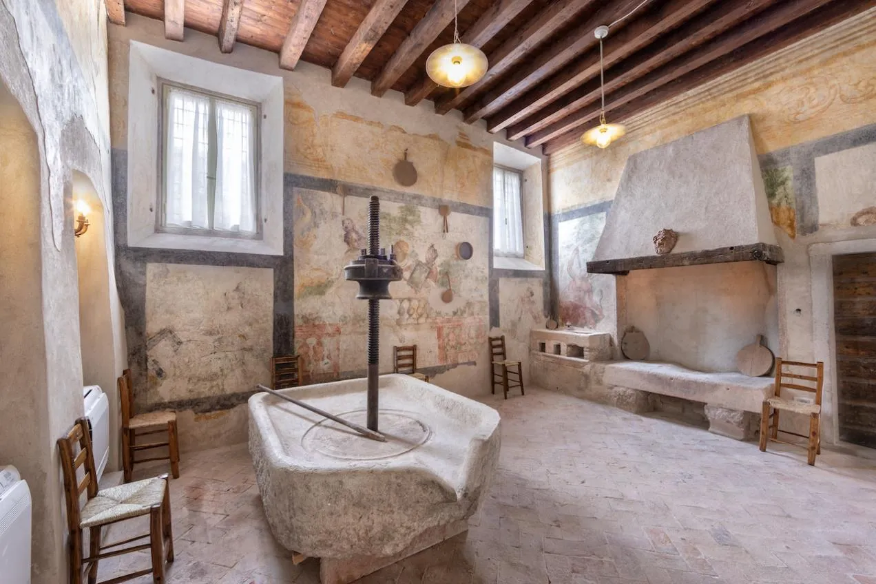 Cucina con antico torchio per uva, pareti affrescate e soffitto con travi a vista in legno