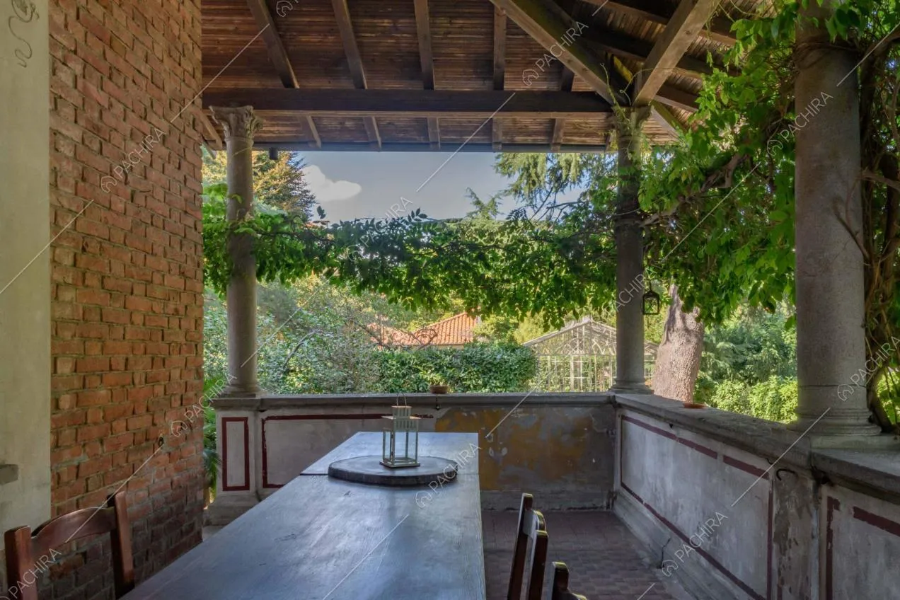Lungo tavolo da pranzo in legno nella veranda, balconata affrescata ed esterni della location in mattoni a vista
