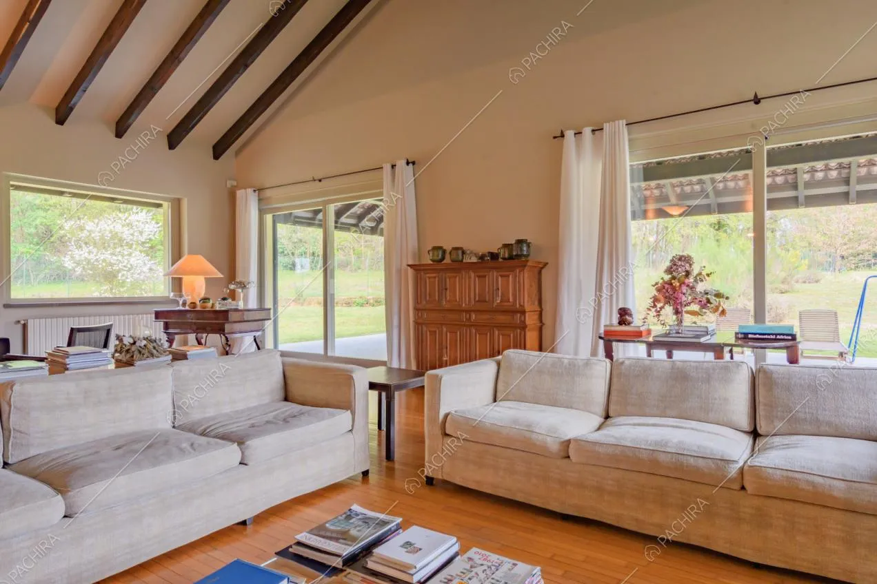 Divani bianchi nella luminosa sala con pavimento in parquet e vista sul giardino tramite le vetrate