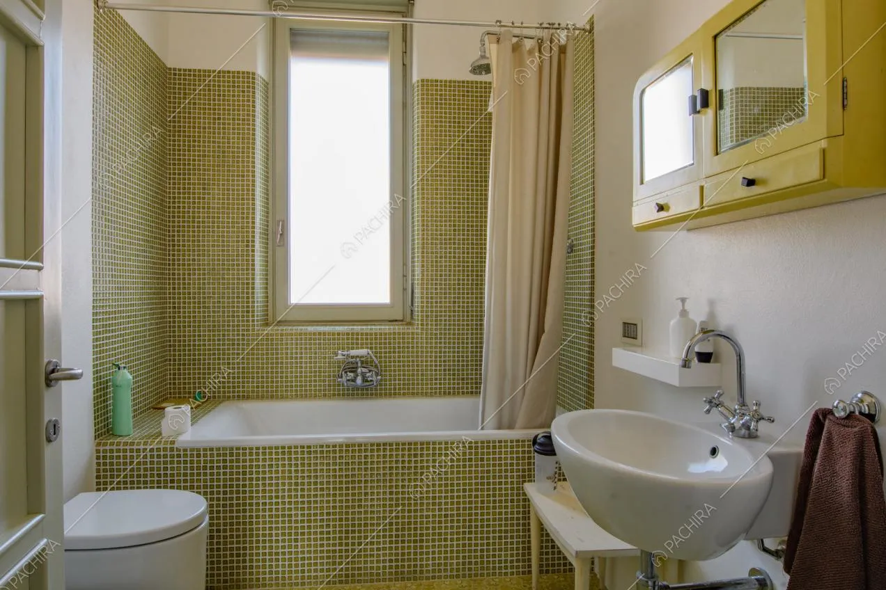 Luminoso bagno con grande vasca e pareti in piccole piastrelle verdi