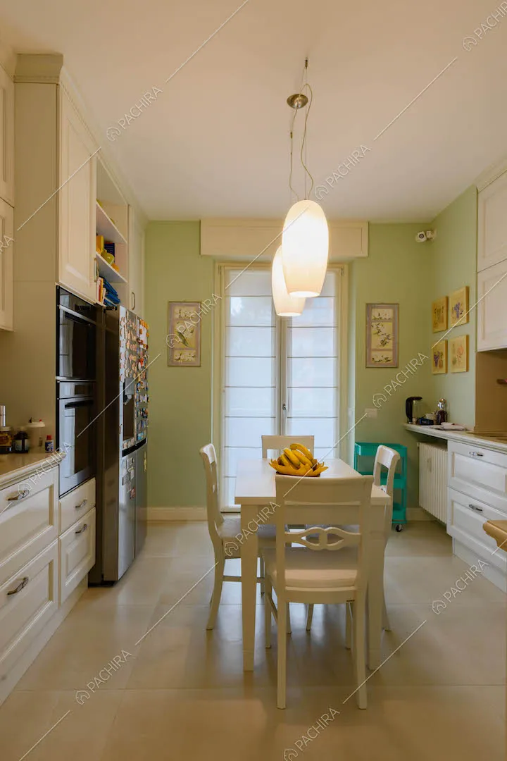Cucina con parete verde, tavolo da pranzo bianco e porta-finestra