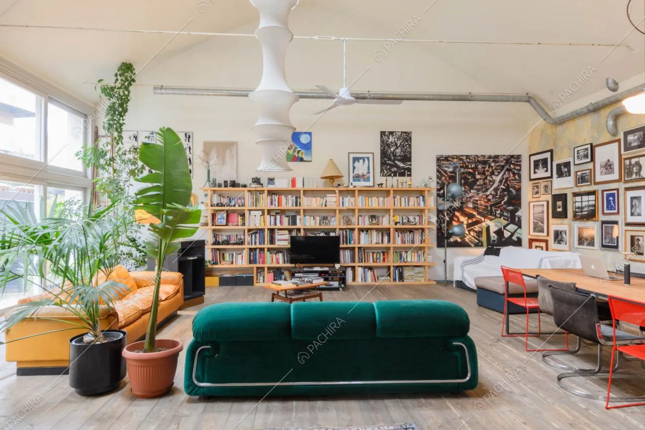 Luminoso salotto con pavimento in parquet, divano verde in velluto e libreria