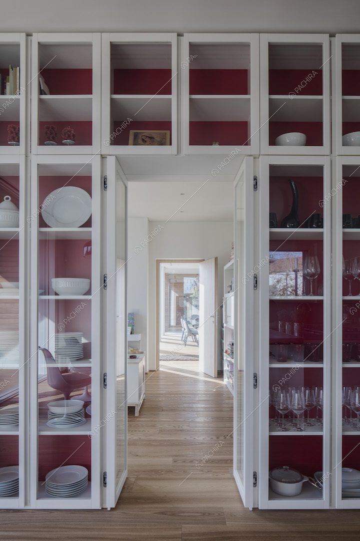 Nella cucina con il pavimento in parquet, parete rossa con credenza a tutta parete in vetro