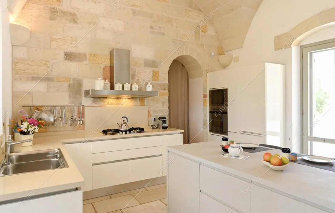 Ampia cucina bianca dai toni chiari con isola, fornelli a gas e porta-finestra bianca
