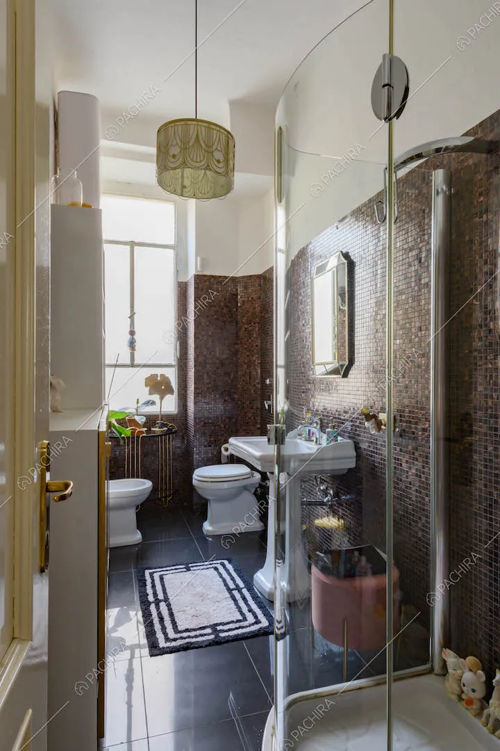 Bagno con box doccia, pavimento nero e pareti in piccole piastrelle dalle nuances marroni
