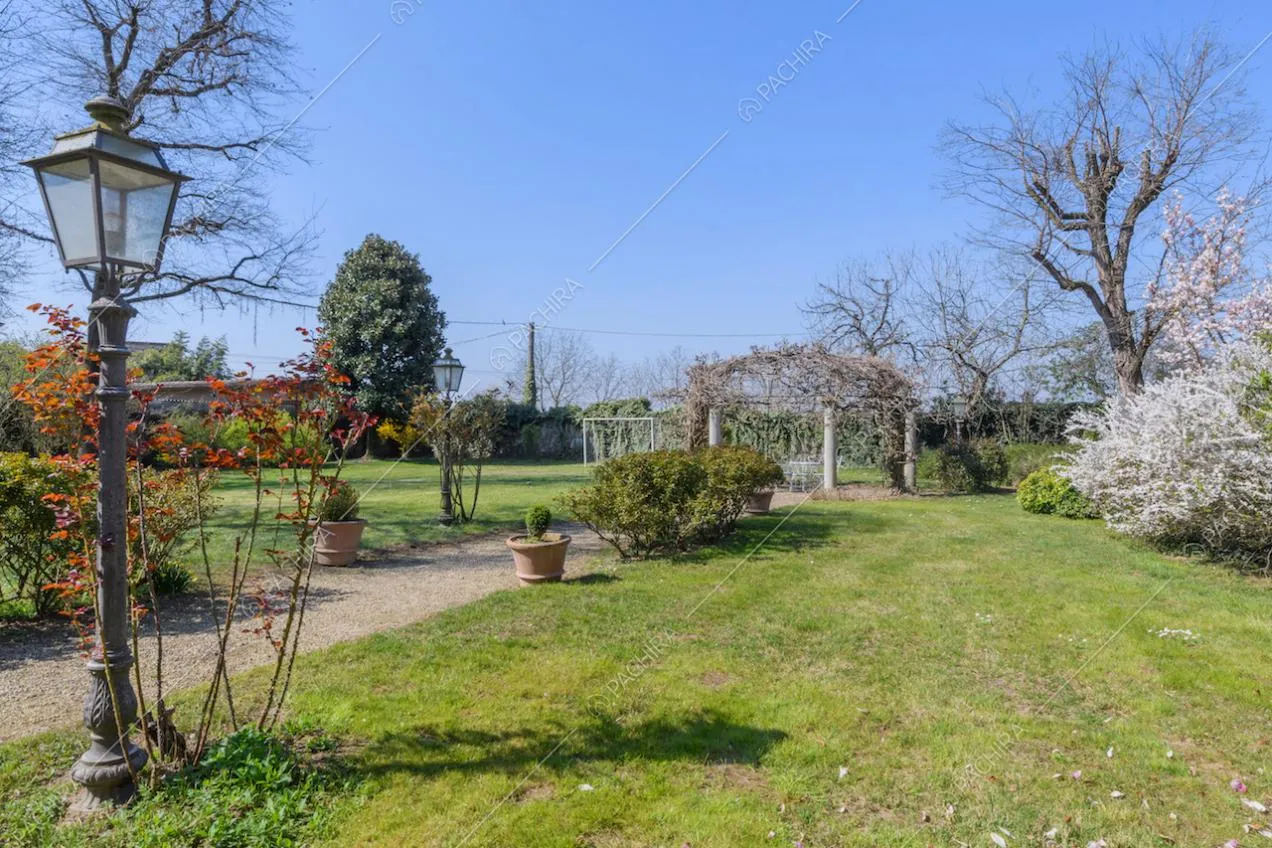 Grande giardino con vialetto, piante e vista sul gazebo con colonne e rampicanti