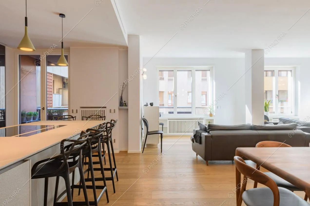 Luminosa zona living con sgabelli neri e fornelli a induzione sulla penisola della cucina