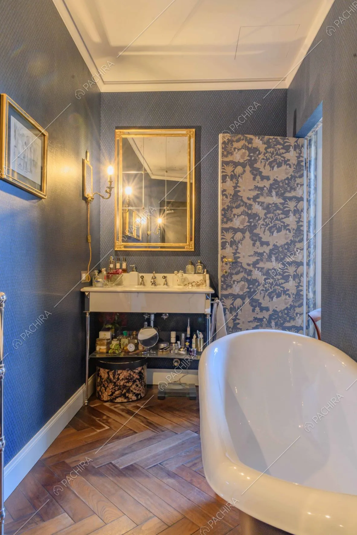 Bagno con vasca, pavimento in parquet, pareti blu e carta da parati sulla porta