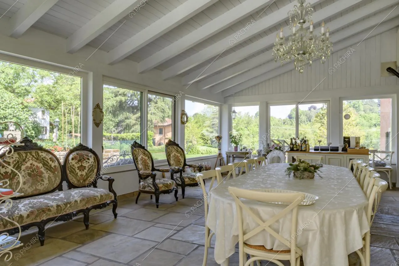 Ampio tavolo da pranzo e divanetti classici, nella veranda illuminata dalle vetrate