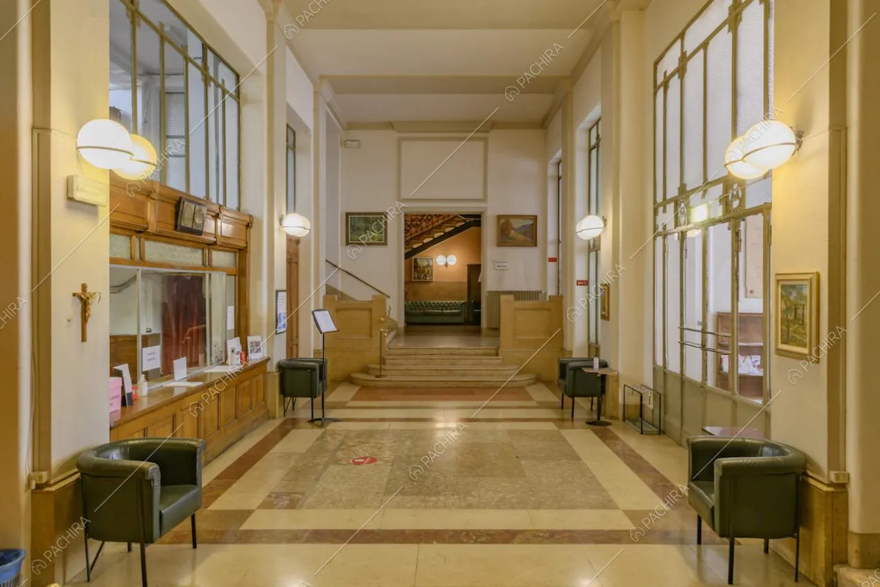 Ampio atrio illuminato da vetrate, poltrone nere, pavimento in marmo e vista su due scalinate 