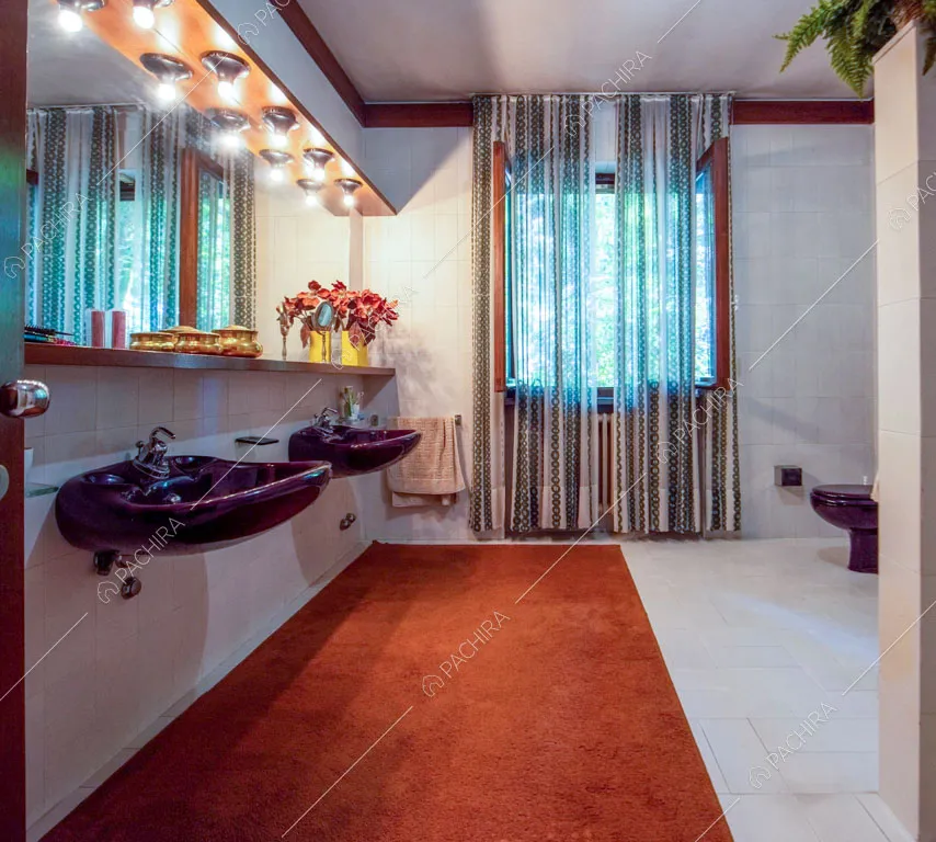 Bagno con sanitari viola, pavimento e pareti bianchi e tappeto arancione