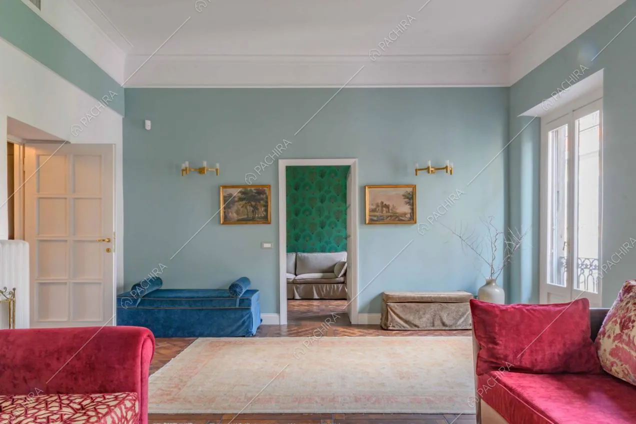 Ampia e luminosa sala con divani in velluto e vista sul salotto con carta da parati verde