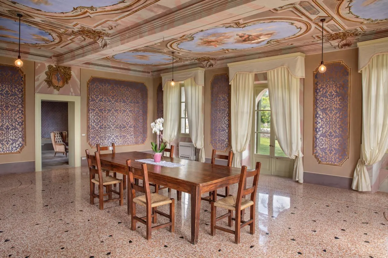 Ampio salone con pavimento in marmo, tavolo da pranzo in legno e soffitto affrescato
