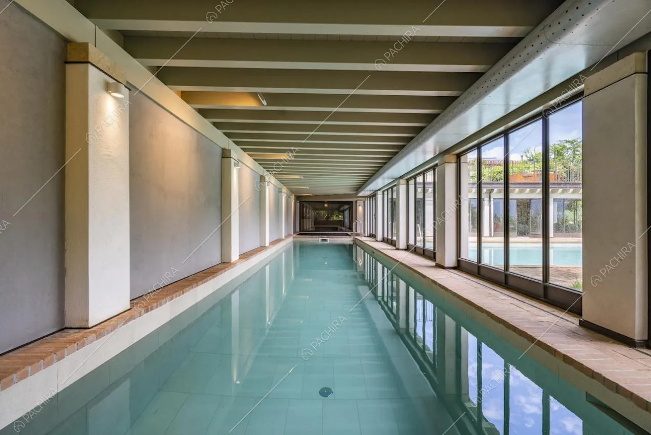 Lunga piscina, pareti con vetrate e soffitto con travi a vista