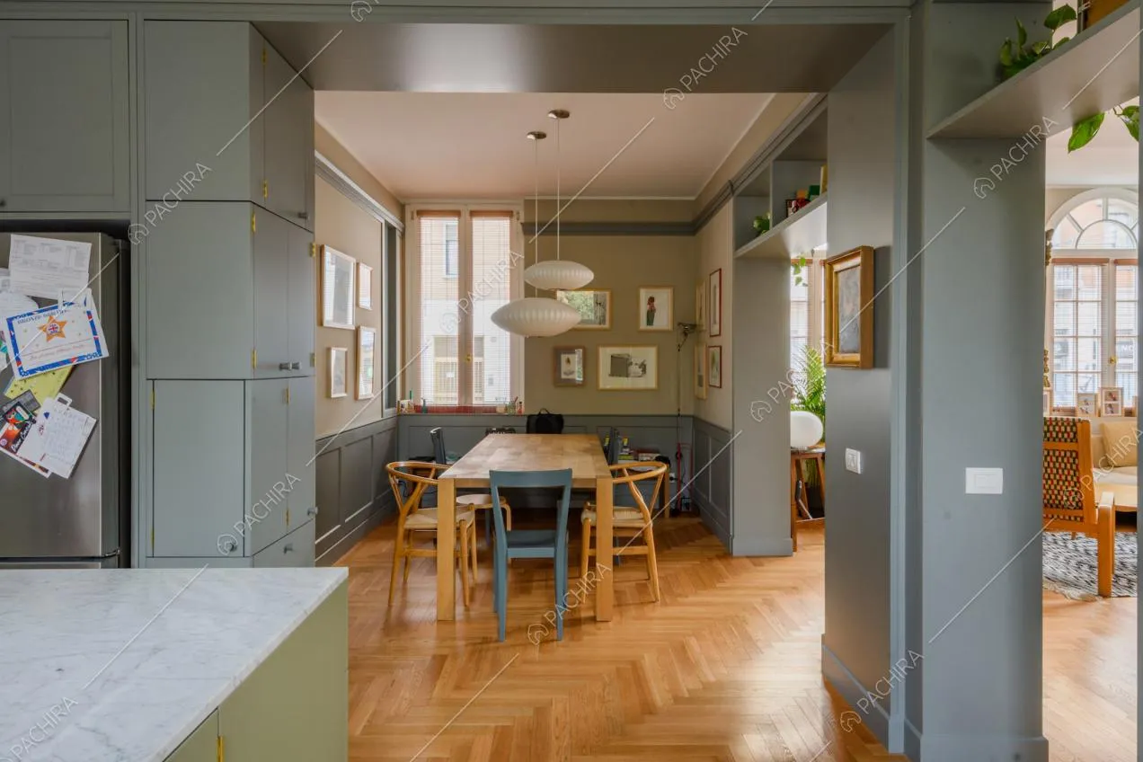 Dalla cucina con penisola vista sulla sala da pranzo con tavolo in legno e pareti beige e blu con boiserie