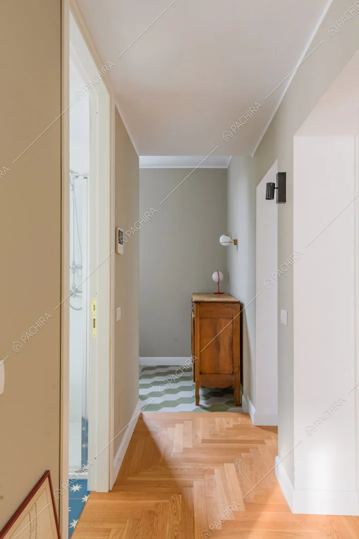 Corridoio con pareti beige e verde chiaro, pavimento in parquet e scorcio sul bagno