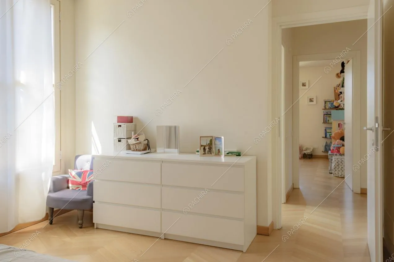 Cassettiera bianca, poltroncina in stoffa su pavimento in parquet
