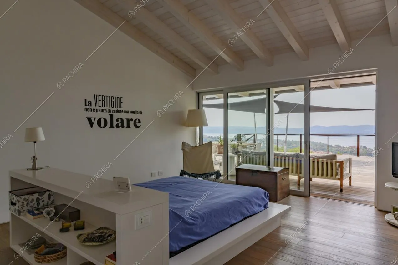 Camera da letto matrimoniale con pareti bianche, soffitto con travi in legno a vista e porte-finestre scorrevoli