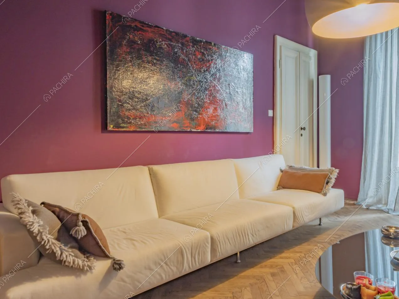 Lungo divano bianco con cuscini e quadro astratto rettangolare appeso alla parete colorata