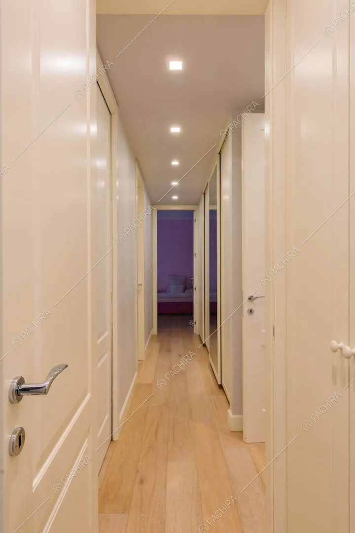 Lungo corridoio con pavimento in parquet e porte bianche con boiserie