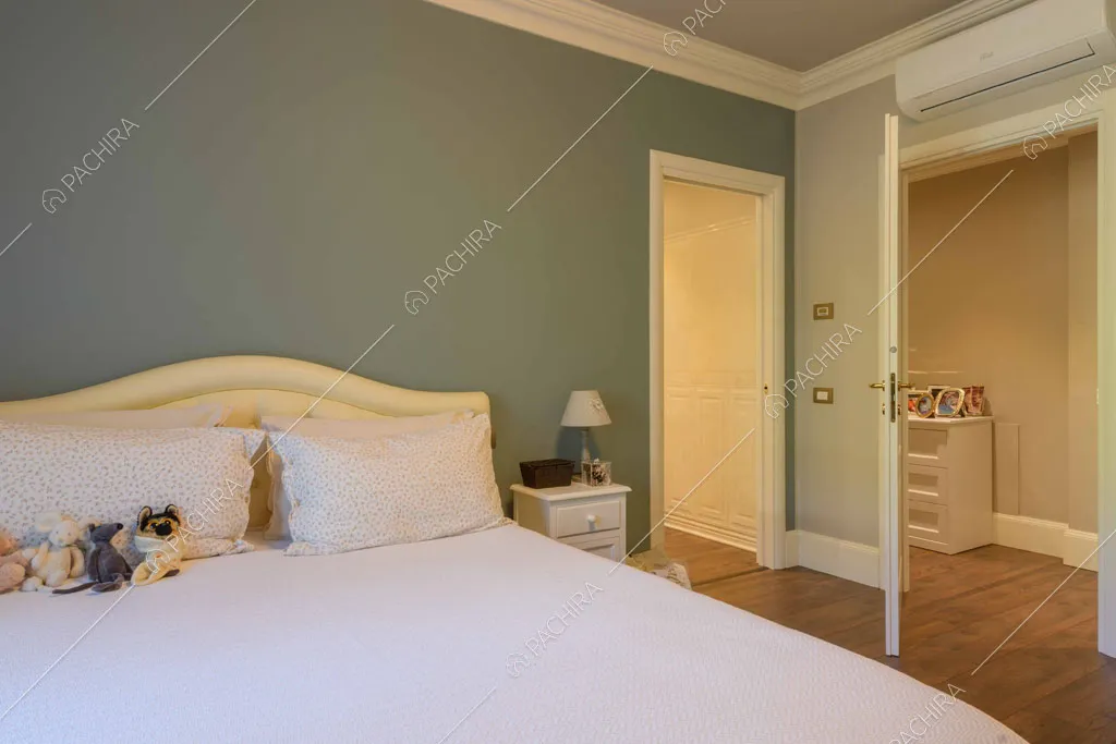 Letto matrimoniale nella camera con parete verdastra e pavimento in parquet