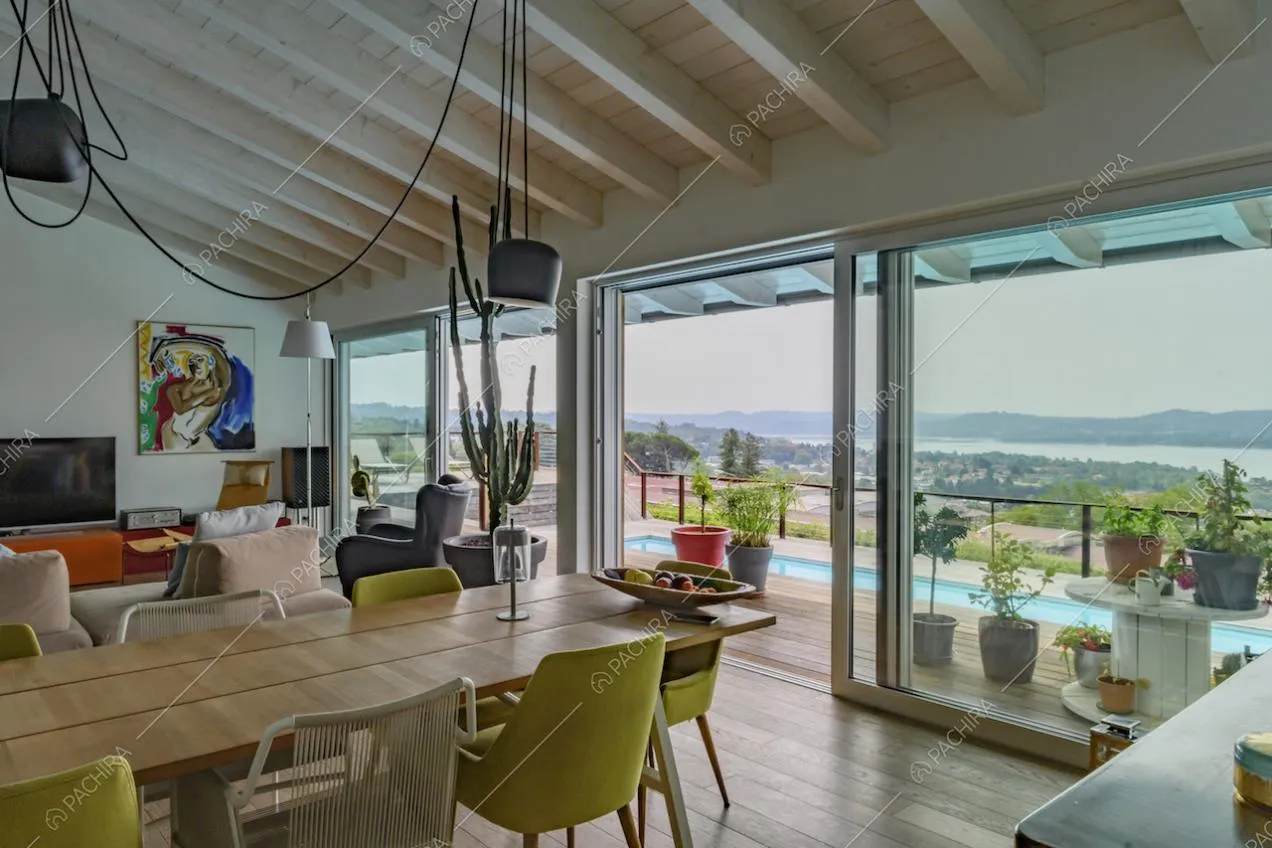 Dalla sala con soffitto in travi in legno, vista sulla terrazza con piscina e sul lago